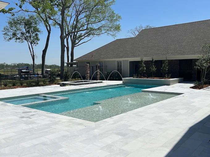 Geometric pool with spa, deck jets and raised planter on a marble deck