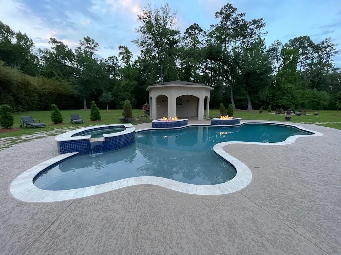 Freeform gunite pool with raised spa and fire bowls at dusk