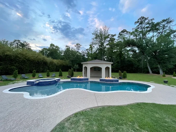 Freeform pool with fire features, raised spa and pool house at sunset