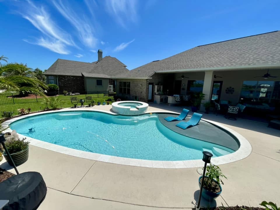 Freeform gunite pool with sun shelf, raised spa and wide concrete decking