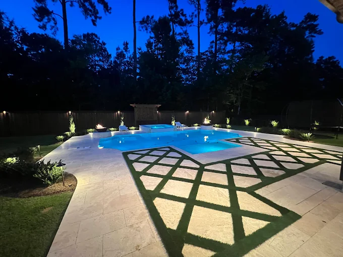 Illuminated pool at night with landscape lighting and turf inlay decking