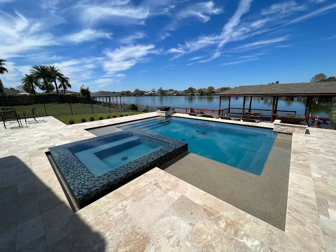 Custom gunite pool and spa overlooking a lake with travertine decking