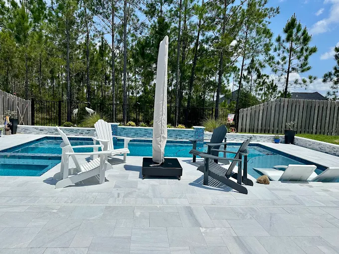Freeform pool and spa with travertine deck, loungers and pine tree backdrop