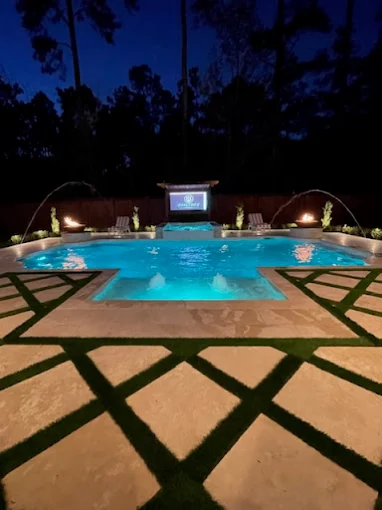 Illuminated pool at night with deck jets, fire features and outdoor screen
