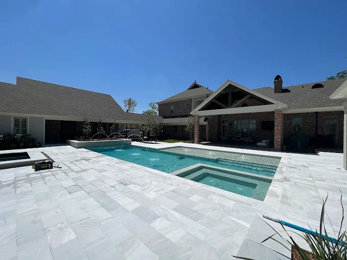 Rectangular pool and spa with deck jets and wide marble paver patio