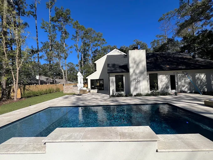 Rectangular pool with tanning ledge beside a white modern Northshore home