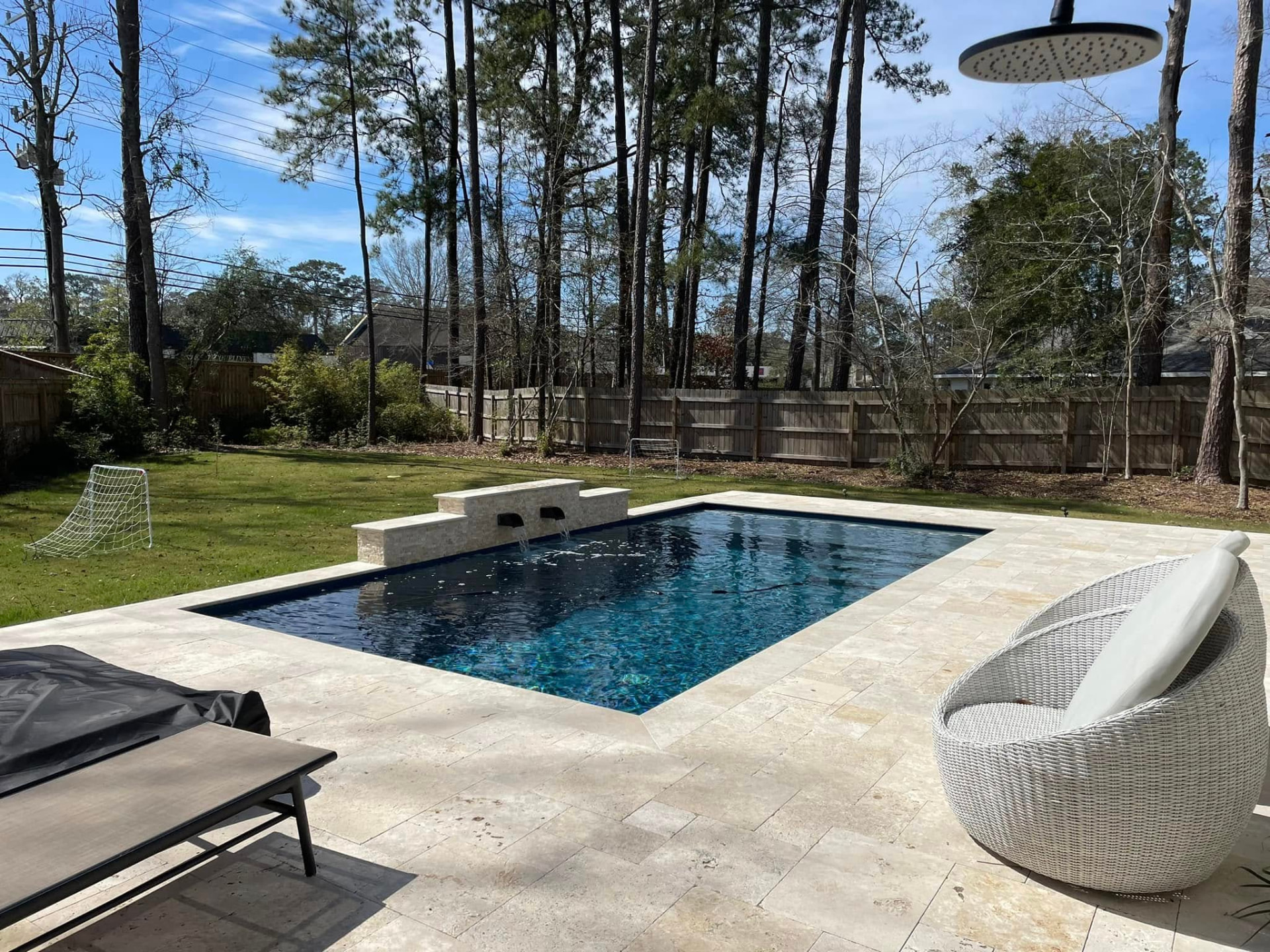 Dark-water rectangular pool with stone scupper wall in a wooded backyard