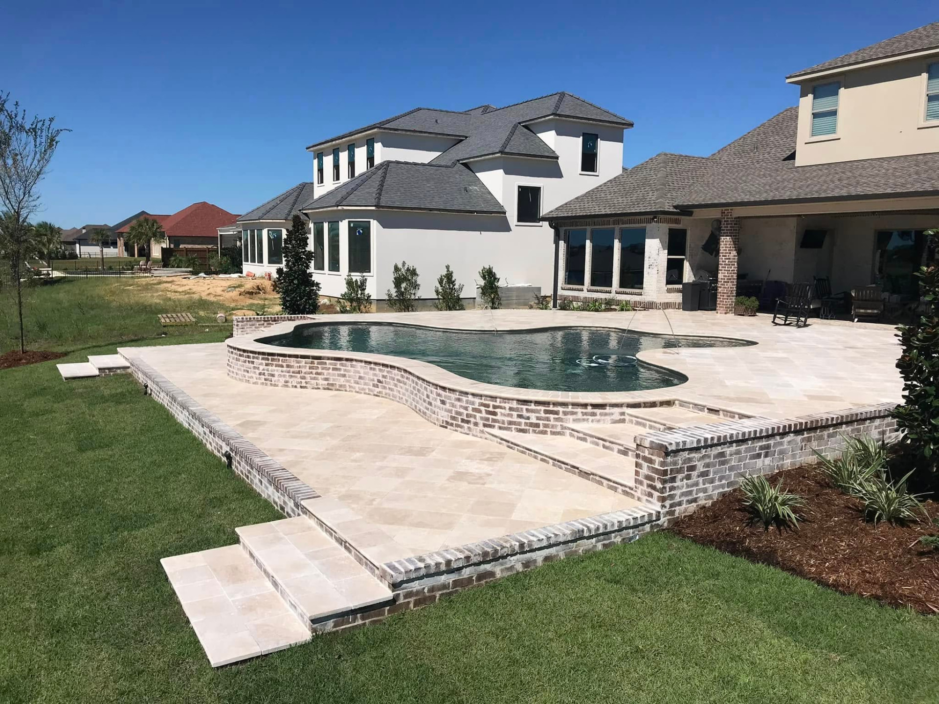 Freeform pool with brick retaining walls, deck jets and travertine patio