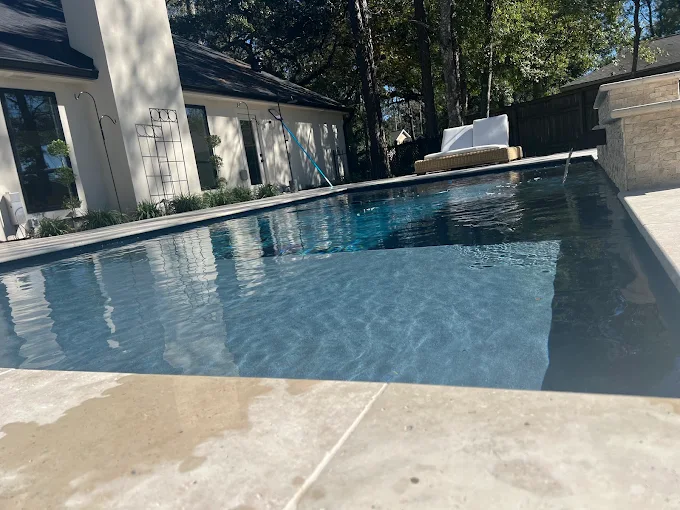 Dark-water rectangular pool beside a modern white home under mature trees