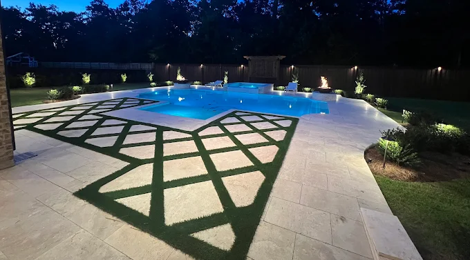 Night-lit pool and spa with fire bowls and turf inlay paver decking