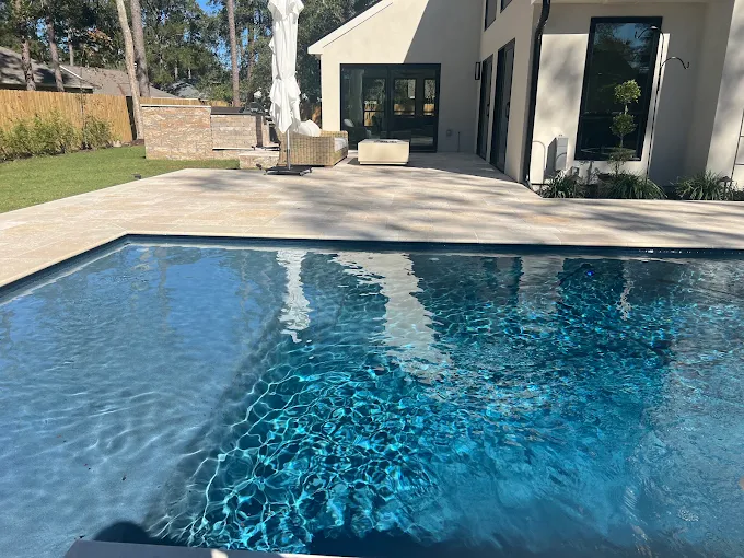 Modern gunite pool with dark interior finish beside a white stucco home