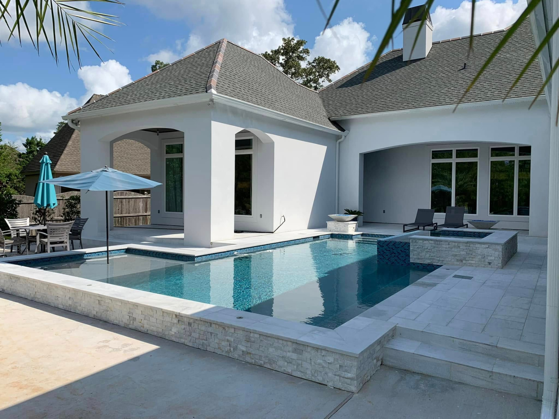 Geometric pool and spa with glass tile accents beside a covered patio