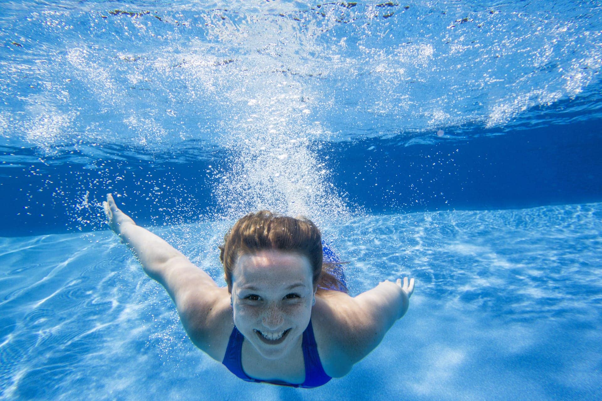 child-swims-underwater-with-smile-in-blue-pool
